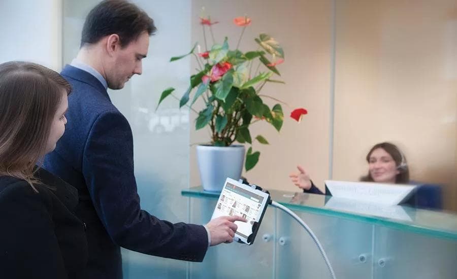 Two visitors registering on a self-service check-in tablet at a corporate reception desk